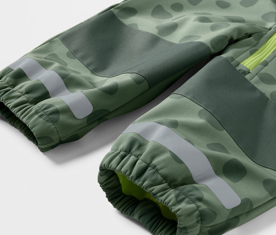 Egy zöld terepmintás gyermek softshell kezeslábas részletgazdag képe, fényvisszaverő csíkokkal és elasztikus mandzsettákkal.