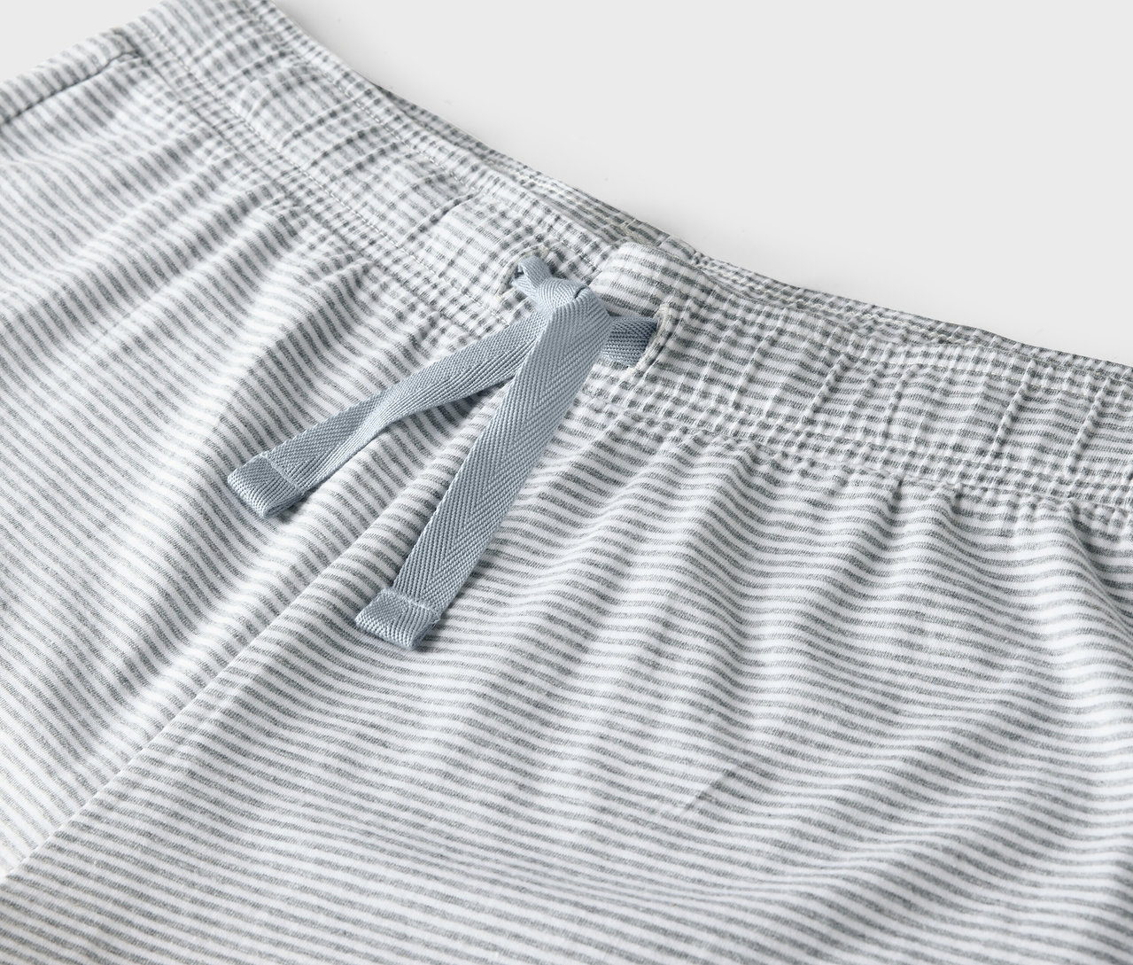Egy szürke-fehér csíkos nadrág részlete kék húzózsinórral a derékrészen.