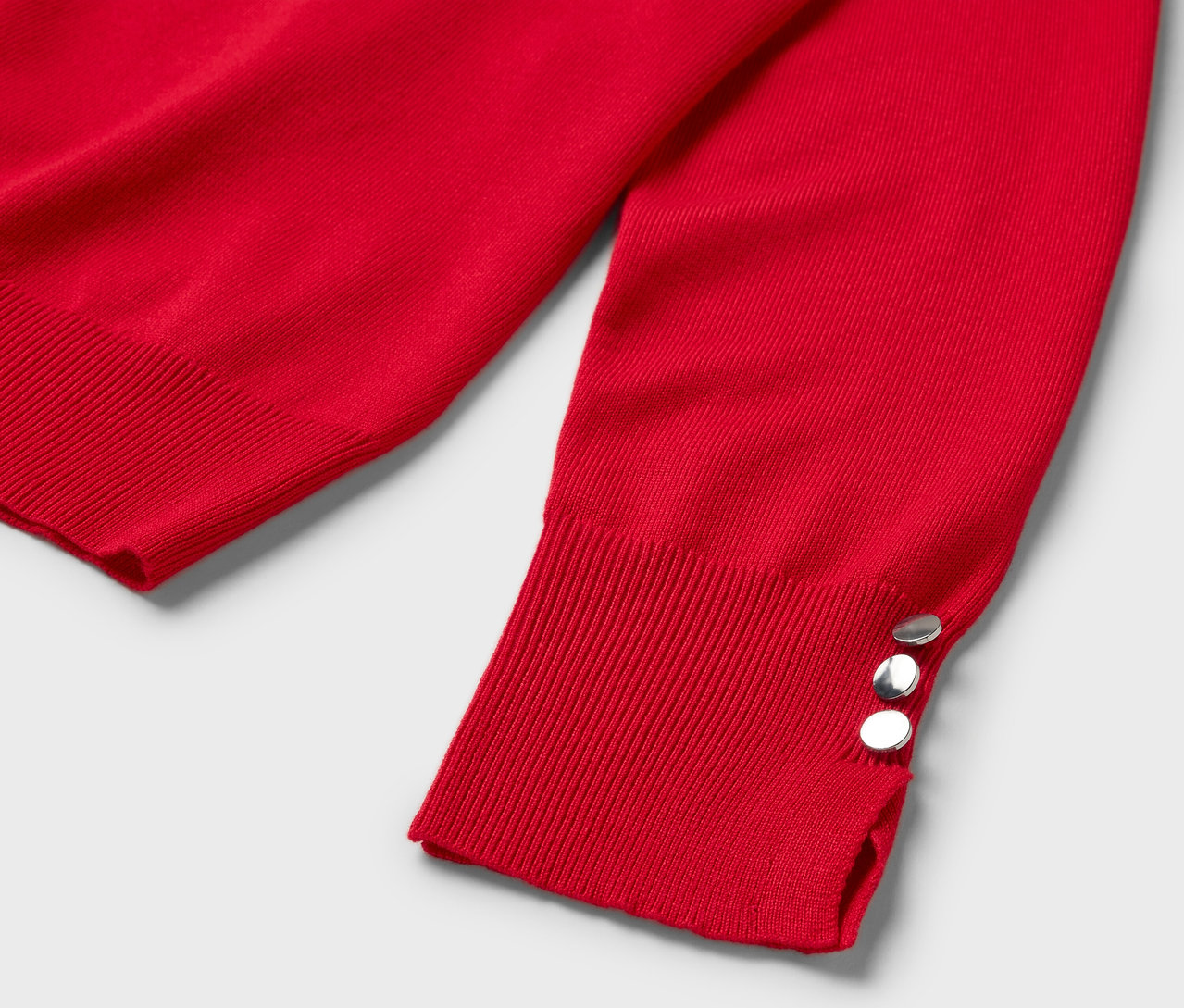 Egy piros, hosszú ujjú pulóver részlete, három ezüst gombbal a mandzsettán.
