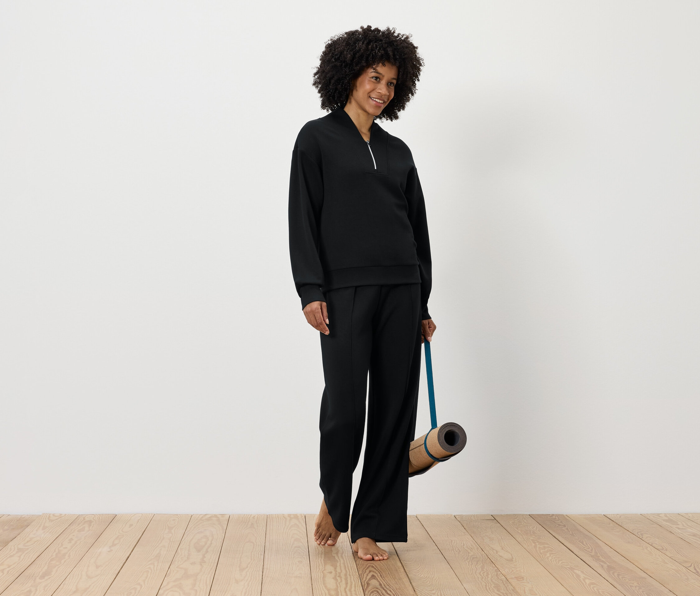 Fekete sportruházatot viselő nő jógamatracot tart.