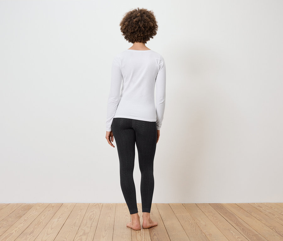 Afro frizurás nő áll háttal, fehér hosszú ujjú pólót és fekete leggingset visel.
