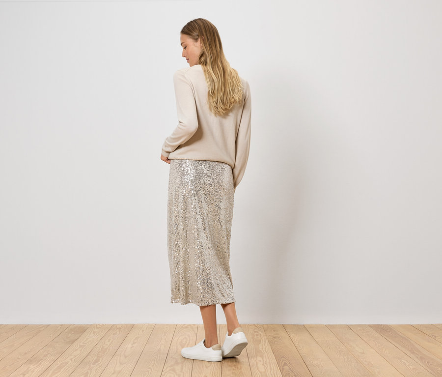 Nő pózol bézs pulóverben és flitteres szoknyában ezüst cipővel.