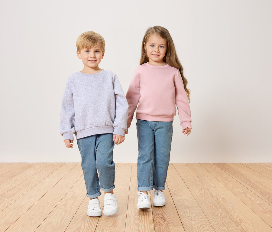 Egy fiú szürke pulóverben és egy lány rózsaszín pulóverben kézen fogva sétálnak.