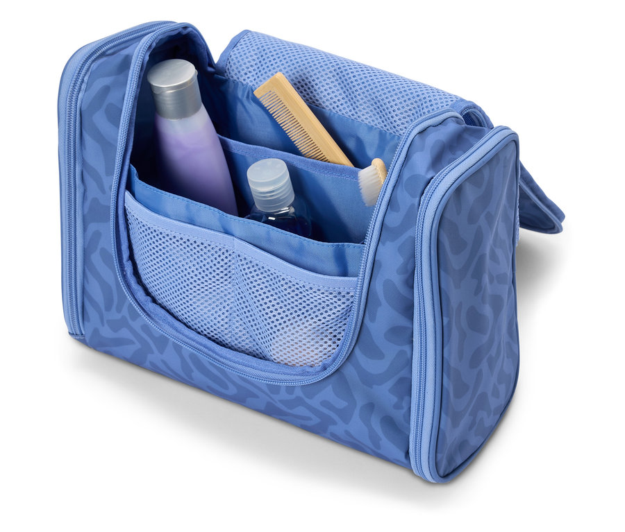 Nyitott, világoskék kozmetikai táska különféle utazási kellékekkel, például samponnal, fésűvel és fogkefével.