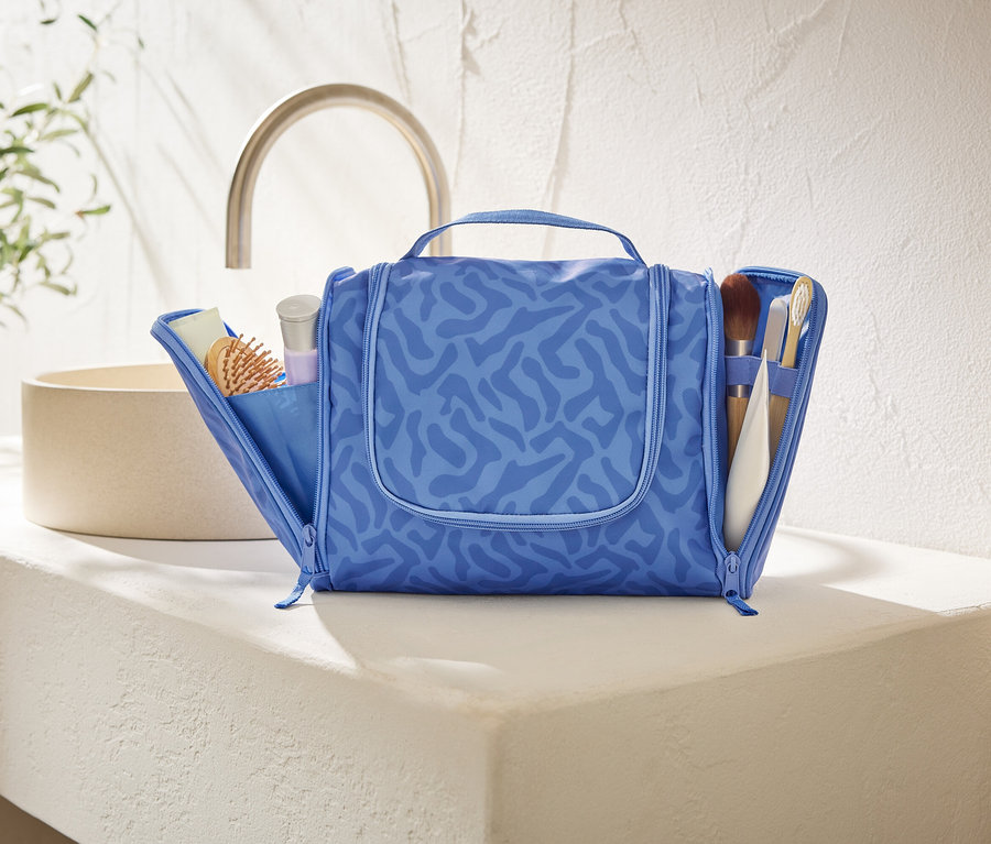 Egy nyitott, kék, absztrakt mintás kozmetikai táska áll egy fehér pulton a fürdőszobában.