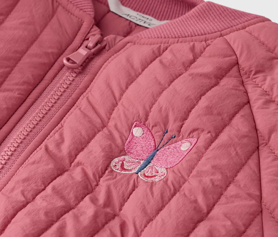 Közeli kép egy rózsaszín, steppelt kabátról cipzárral és hímzett pillangóval.