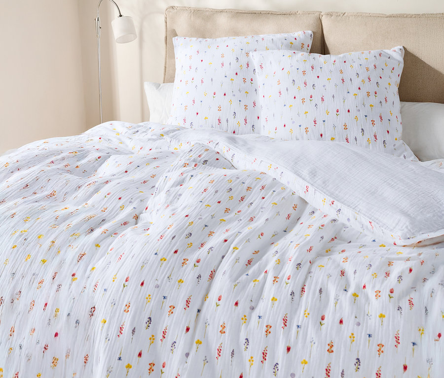 Egy virágmintás, fehér ágyneművel és párnákkal borított ágy közeli képe.