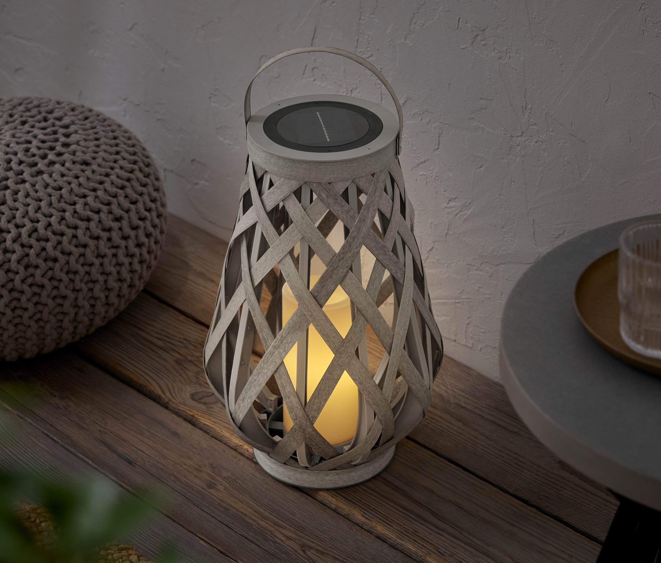 Egy fonott lámpás napelem panellel egy puff mellett áll egy fapadlón.