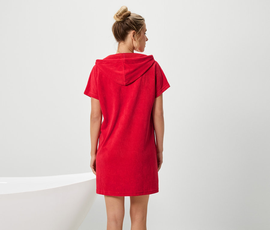 Egy kontyos nő piros, rövid ujjú kapucnis ruhát visel, és egy fürdőkádra néz.