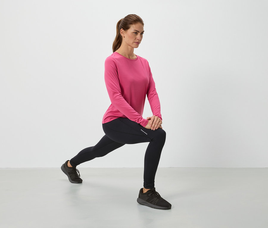 Rózsaszín felsőben és fekete leggingsben lévő nő nyújtózkodik.