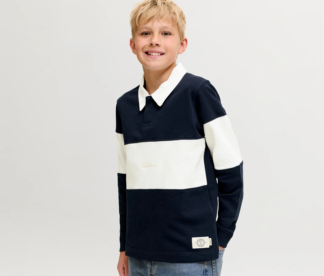 Mosolygó szőke fiú visel egy sötétkék-fehér csíkos Jack&Jones Polo Pulóvert fehér gallérral.