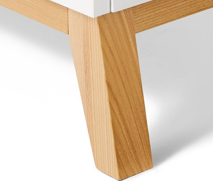 Egy fehér komód részlete világos fa lábakkal.