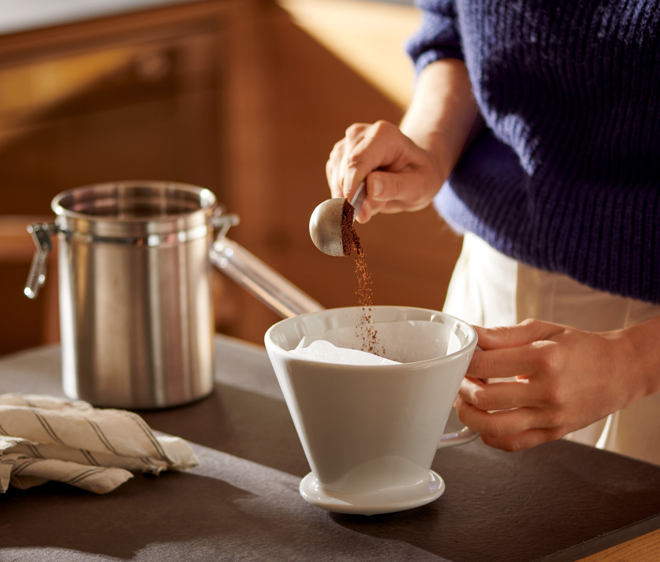 Nő kávét tölt egy fehér, 4-es méretű kézi kávéfilterbe, 4-es méretű papírfilterrel.