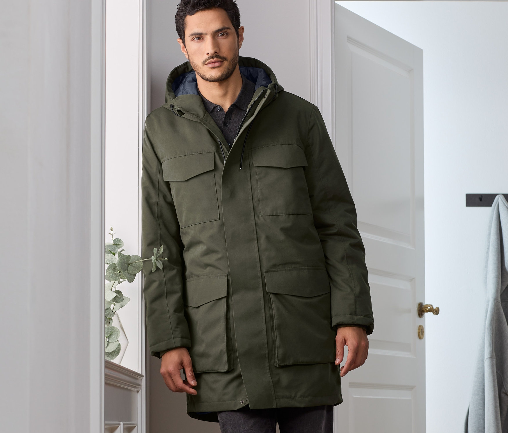 A falnak dőlő férfi olívazöld parkát visel.