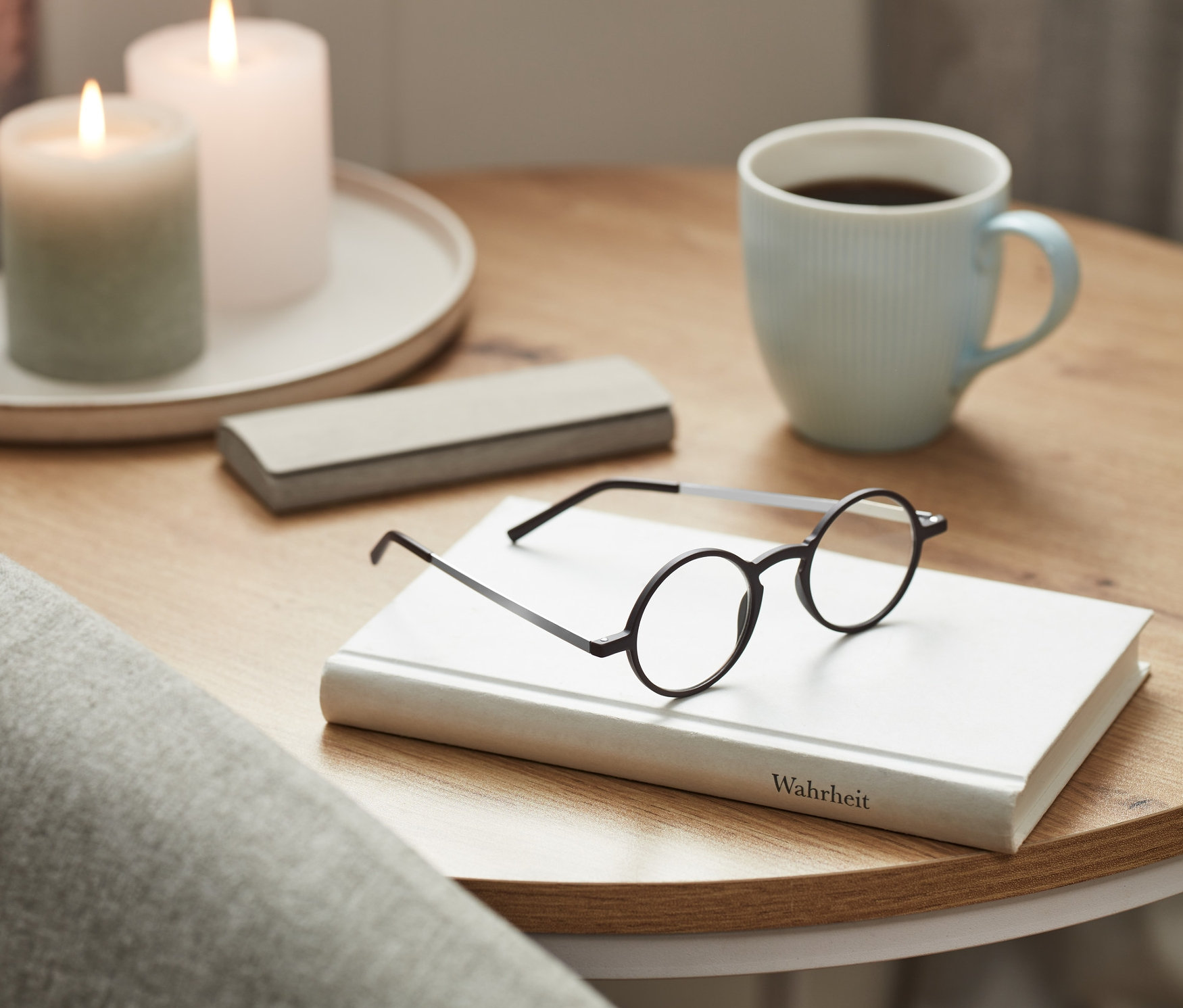 Ultravékony olvasószemüveg tokkal egy könyvön. Az asztalon egy csésze és gyertyák vannak.