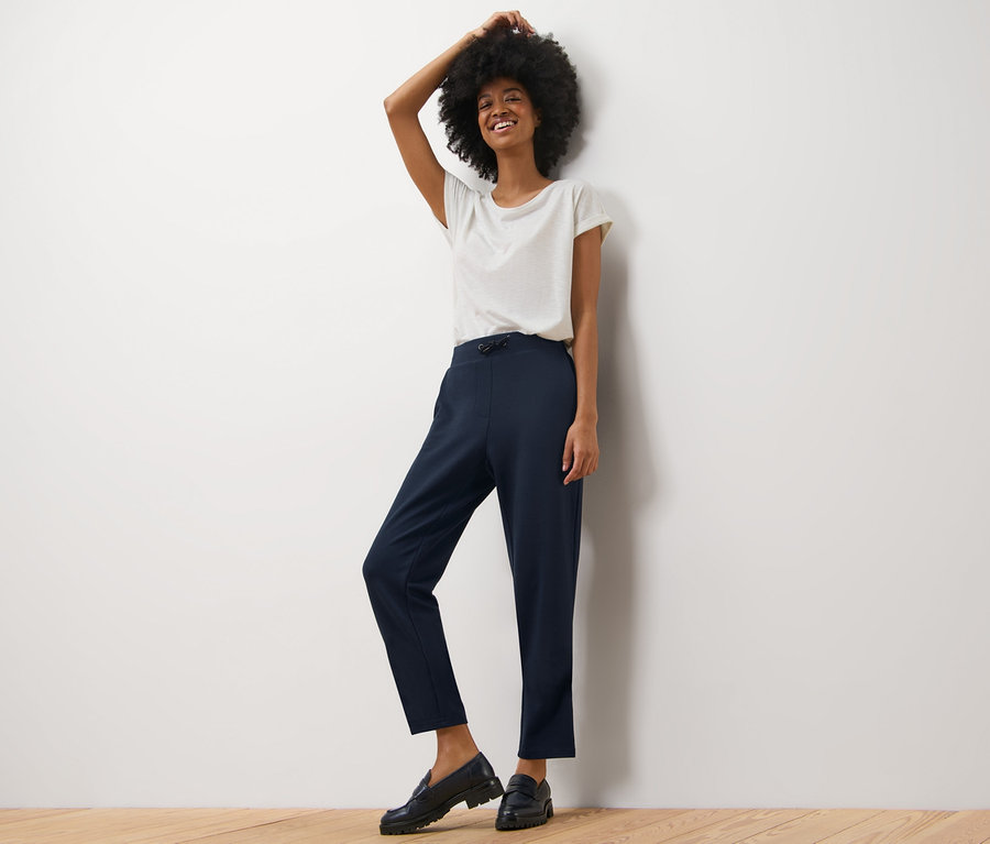 Nő pózol sötétkék szabadidőnadrágban és fehér pólóban.