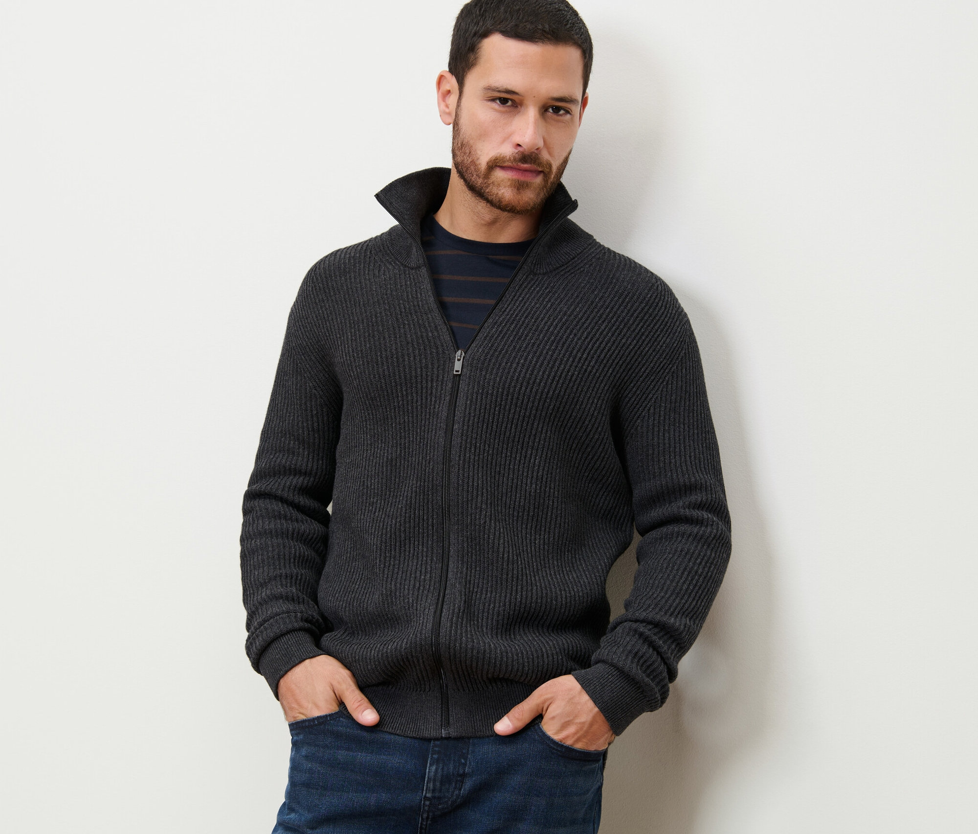 Egy férfi áll zsebre tett kézzel, melírozott antracit kötött kardigánt visel.