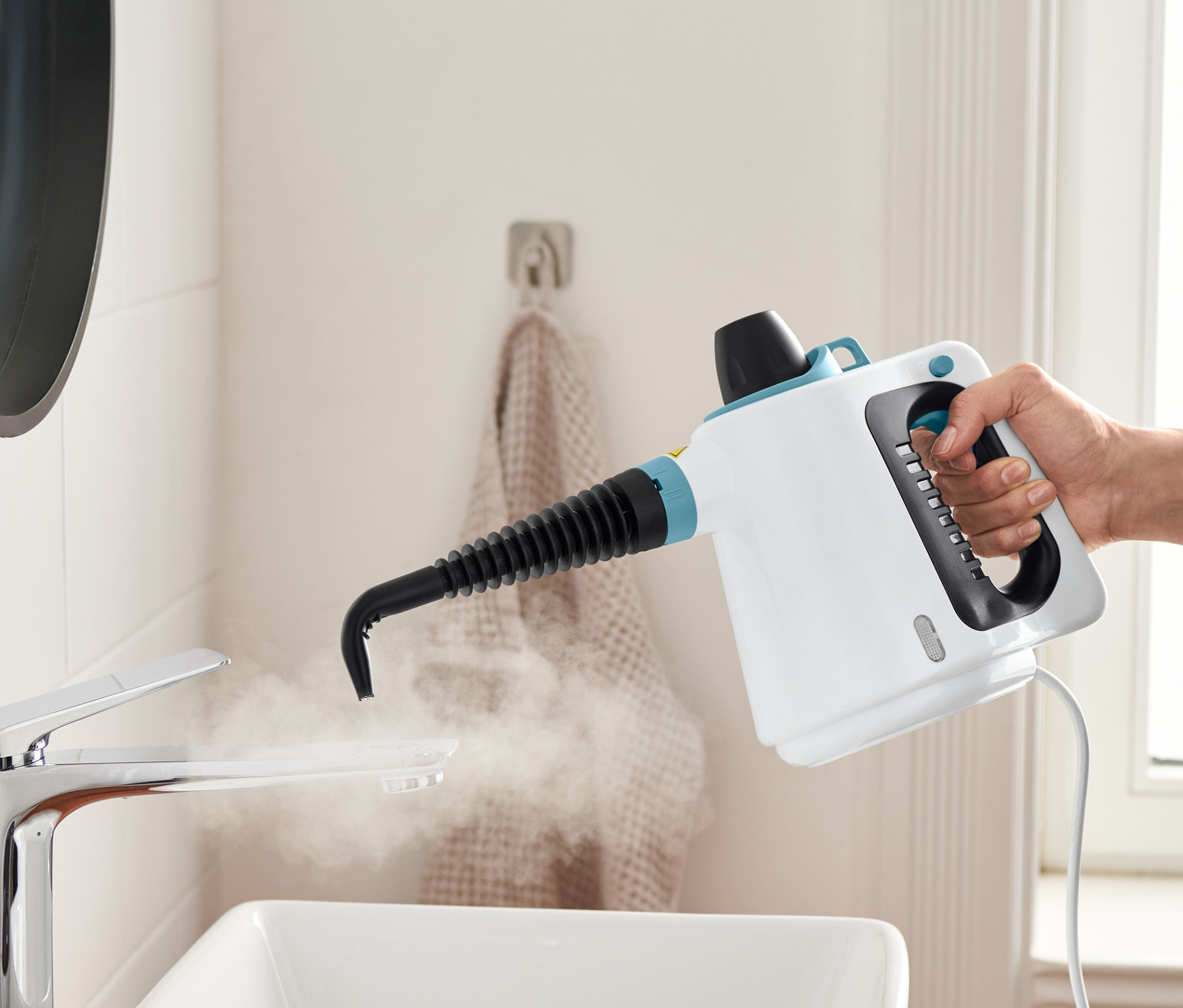 Egy kéz gőztisztítót tart és tisztít vele egy mosdókagylót.