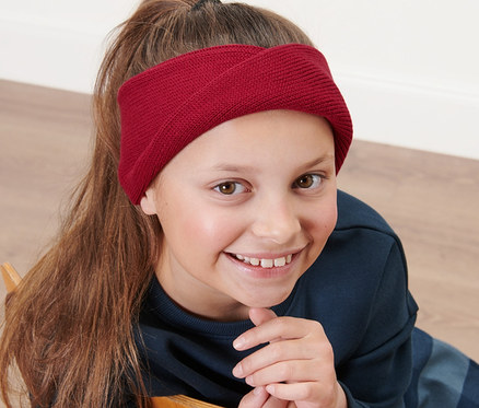 Lány ül egy széken, és kislány kötött fejpántot visel.