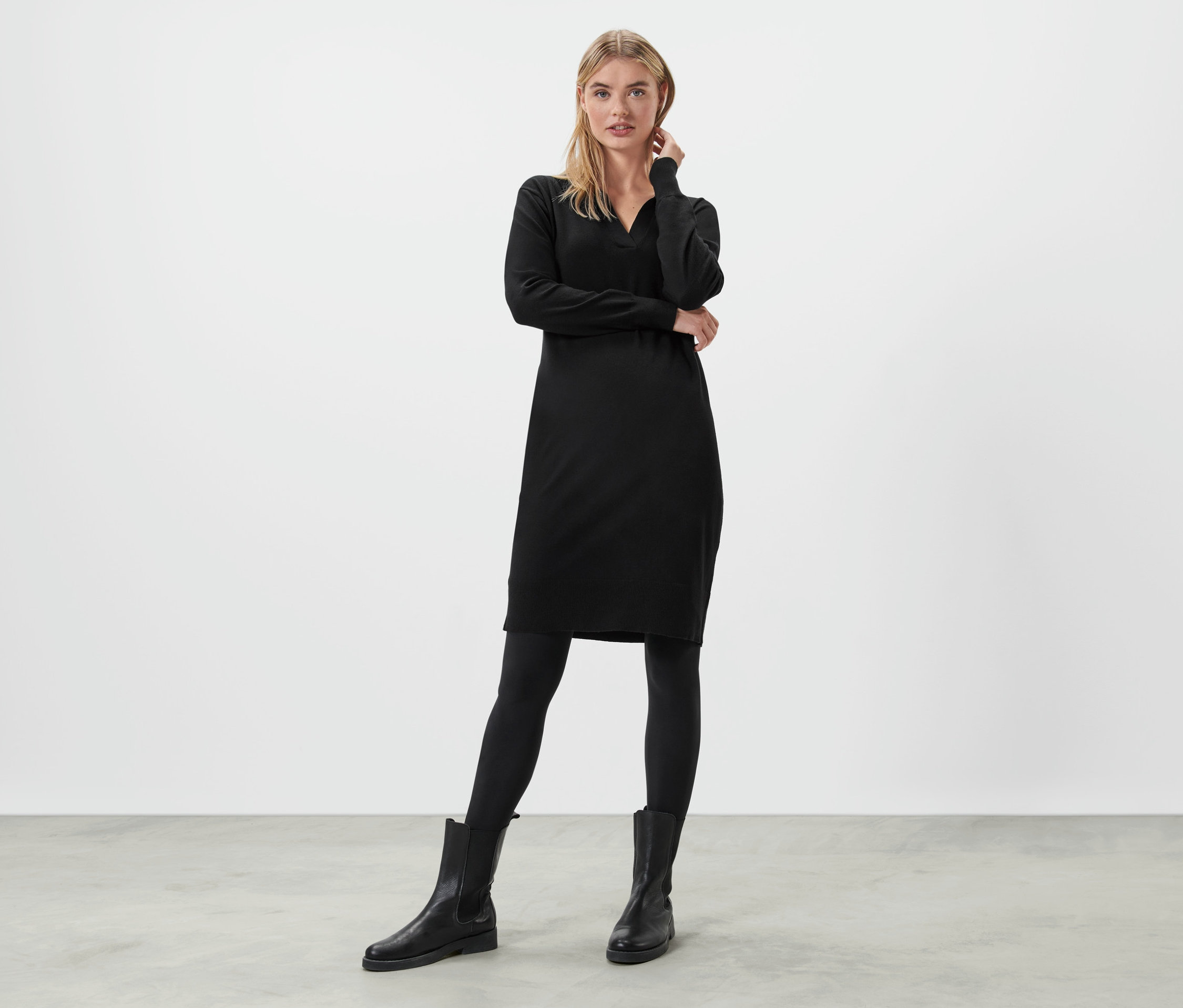 Egy szőke nő áll és pózol egy fekete kötött ruhában.