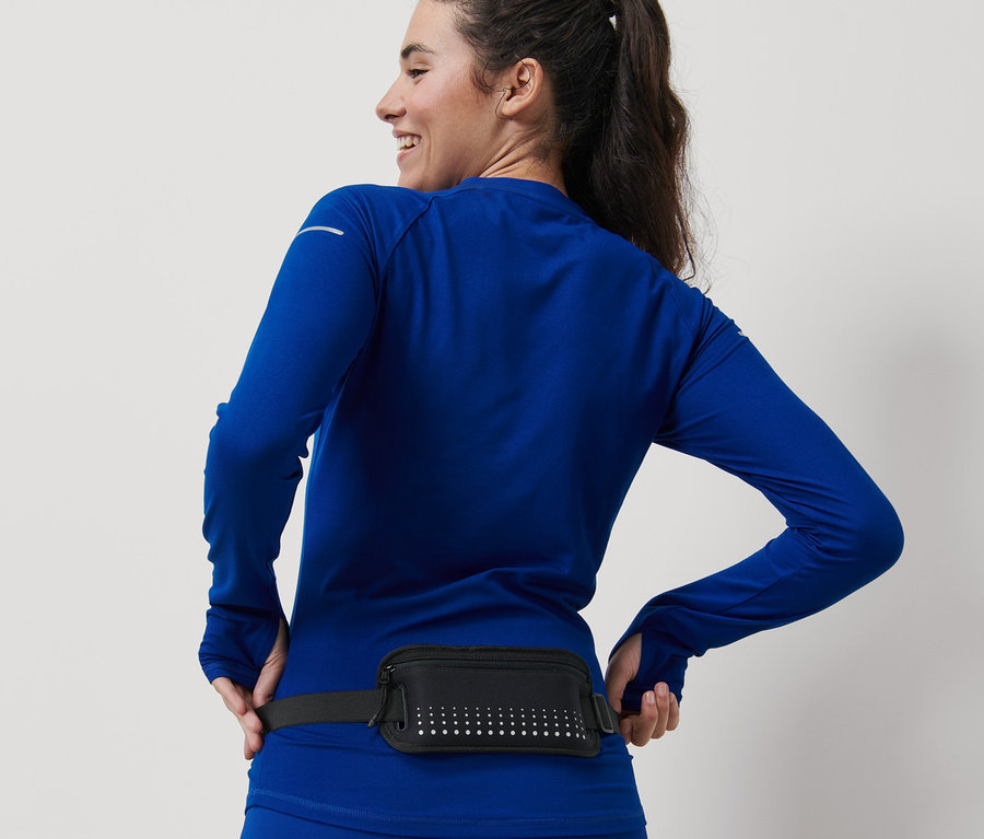 Mosolygó nő kék sportruházatban, fekete futóöv okostelefon-tartóval.
