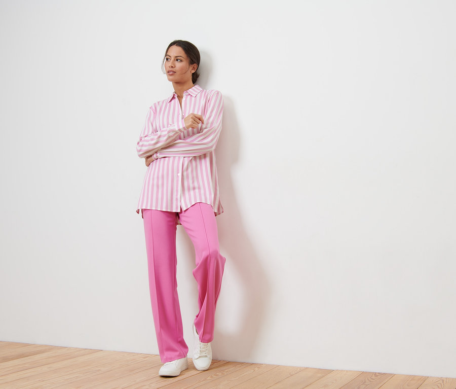Nő pózol rózsaszín nadrágban és csíkos blúzban.