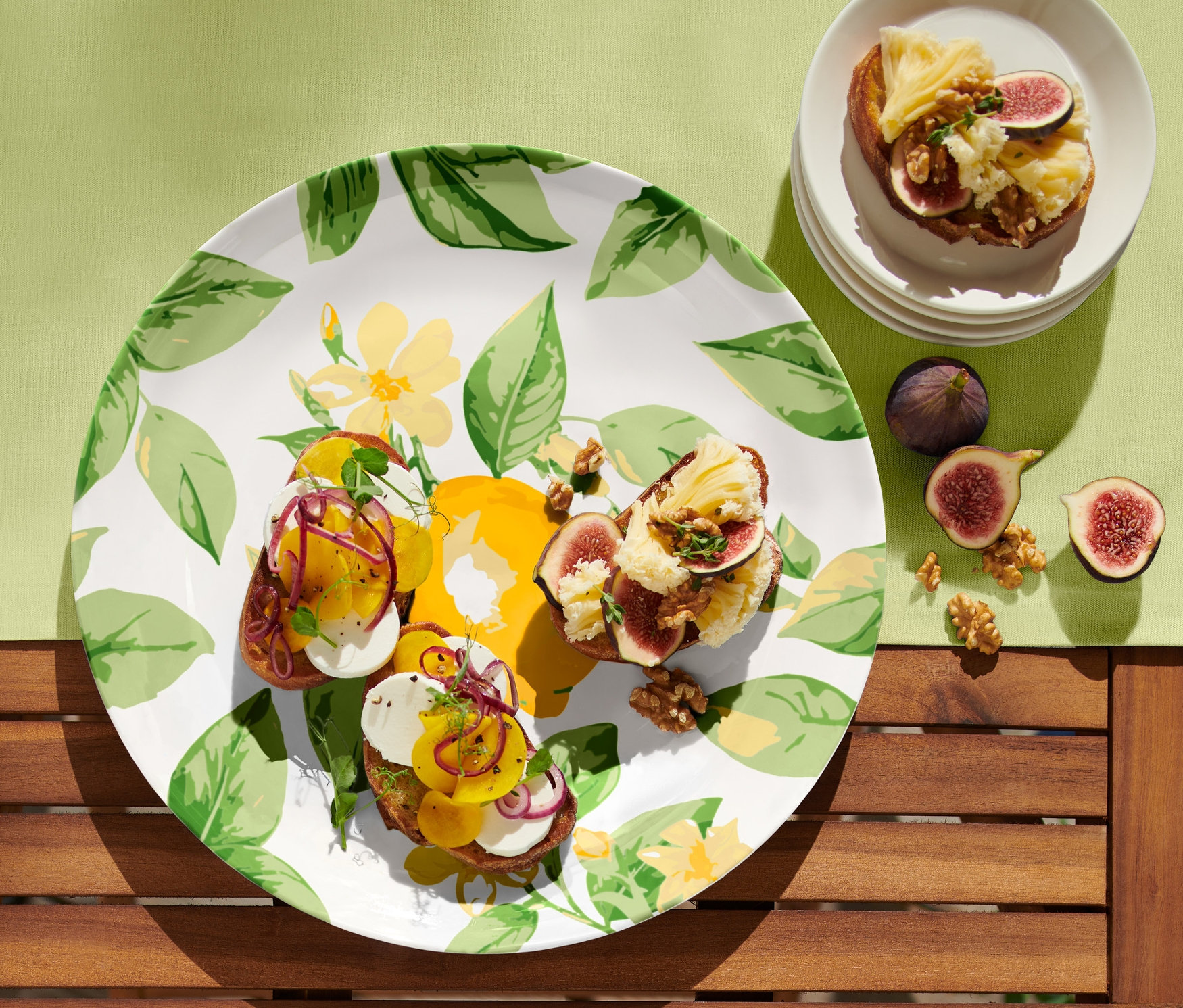 Három fügés-sajtos pirítós egy kínálótálcán. Az asztalon fügék és diók is találhatók.