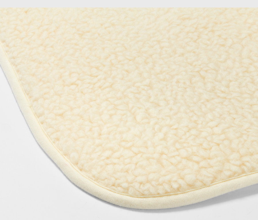 Egy bézs színű, nyírt gyapjú jógamatrac sarkának részlete.