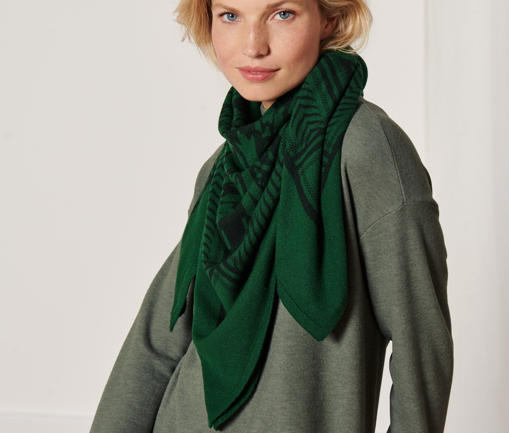 Egy szőke nő mintás, zöld női sálat visel.