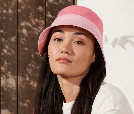 Nő ül egy padon, rózsaszín túrakalap van rajta.