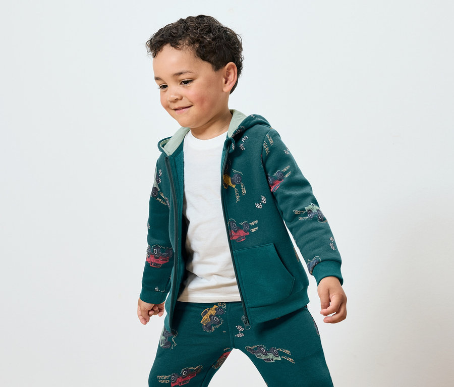 Fiú zöld színű, autós mintás tréningruhában.
