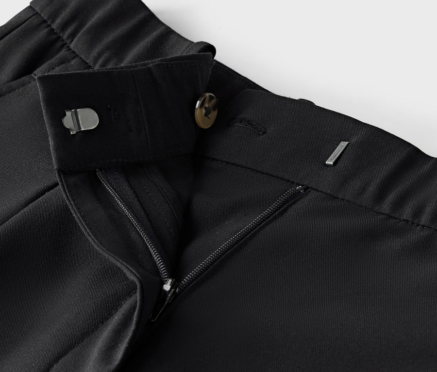 Egy fekete szövetnadrág részlete cipzárral és gombbal.