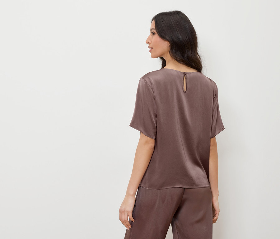 Nő barna szatén felsőben és nadrágban, balra néz.