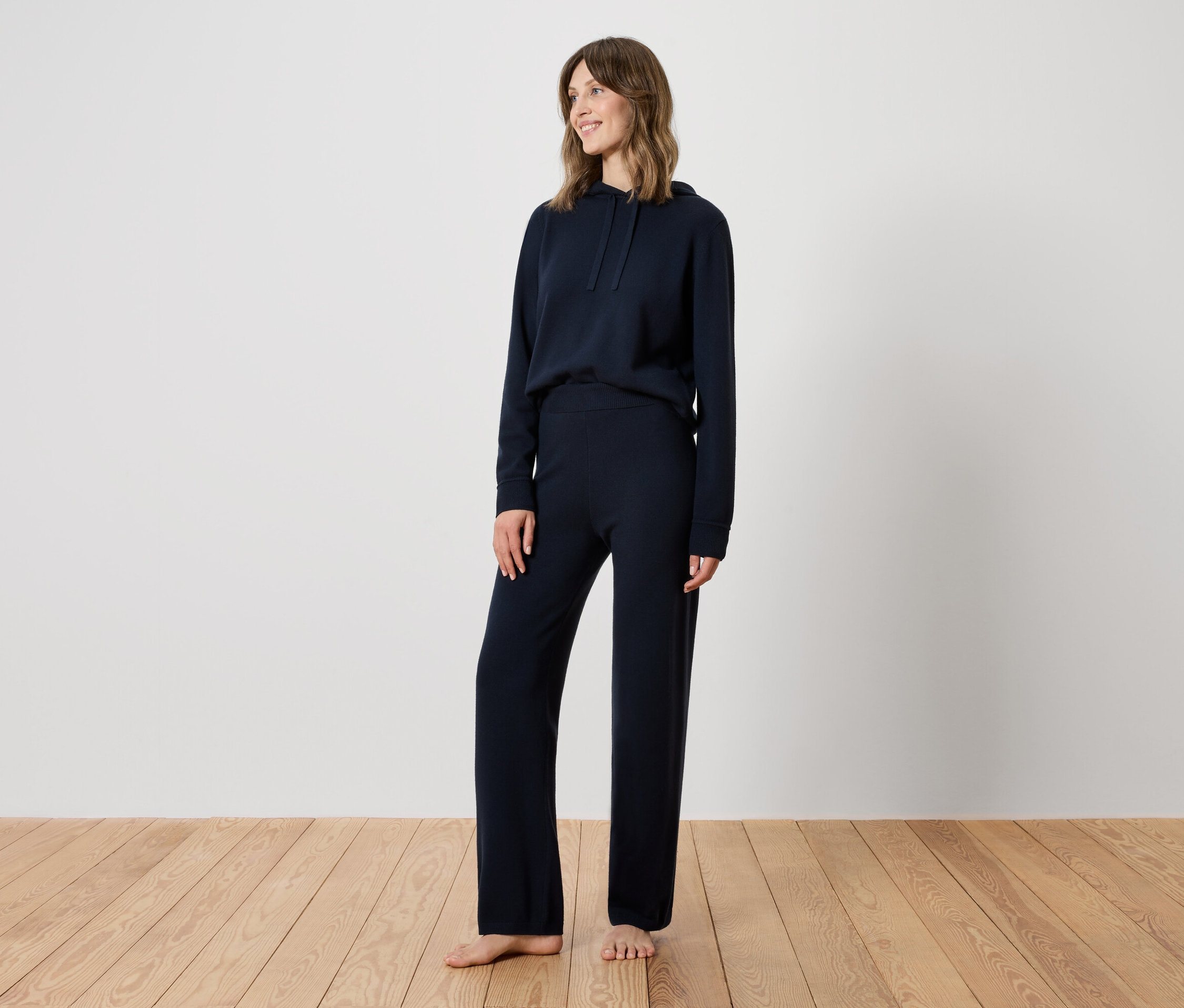 Egy nő áll a fapadlón, sötétkék tréningruhát visel.