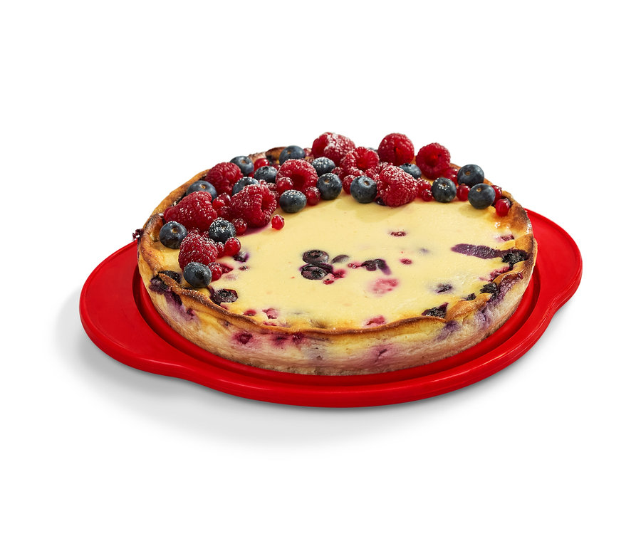 Gyümölcsökkel díszített sütemény egy piros összehajtható süteményformán.