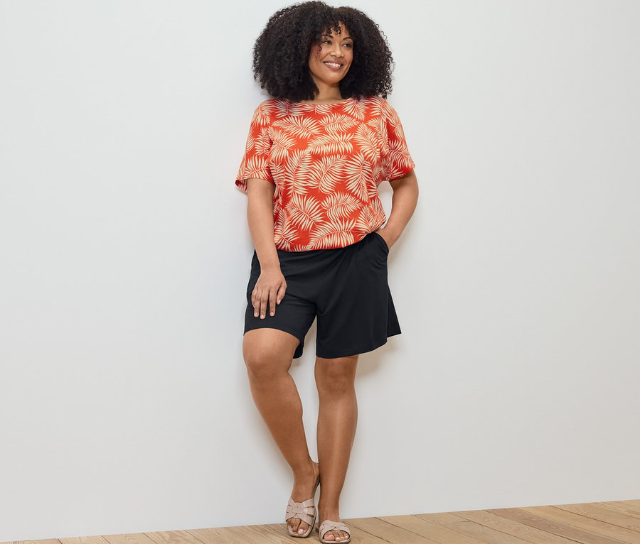 Nő pózol nyomott mintás női pólóblúzban és fekete jersey rövidnadrágban.