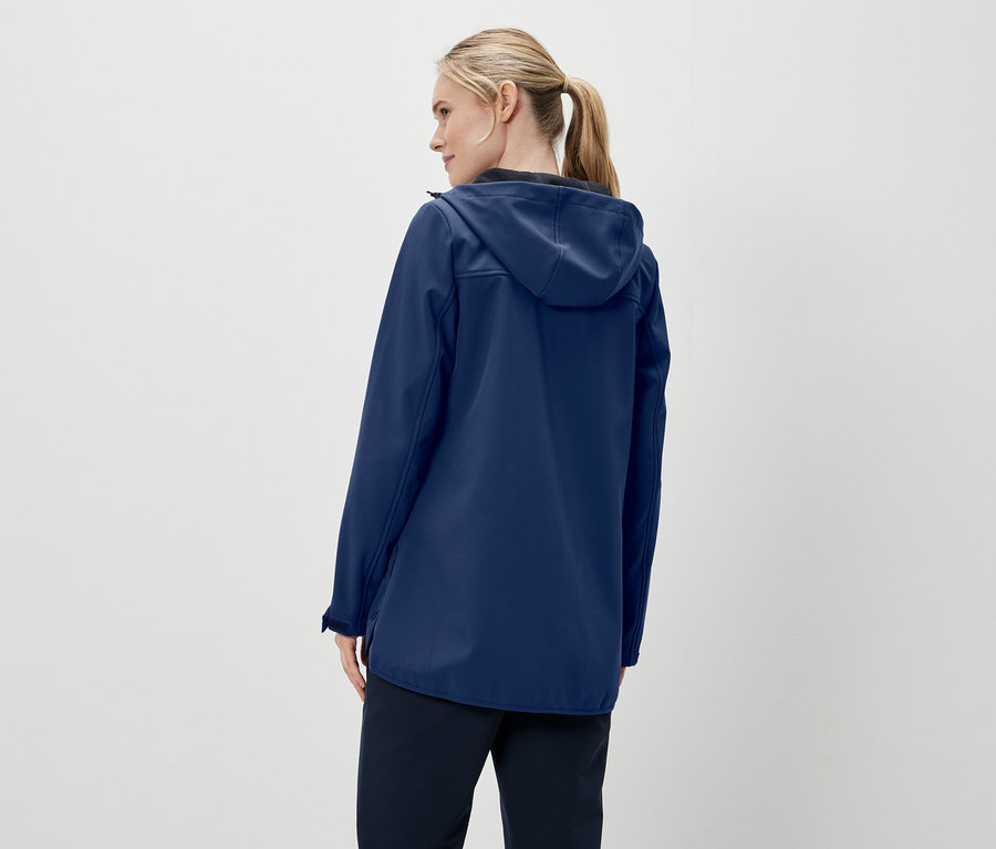 Hátulnézet egy szőke hajú, lófarokba kötött nőről, aki sötétkék kapucnis kabátot és sötét nadrágot visel.