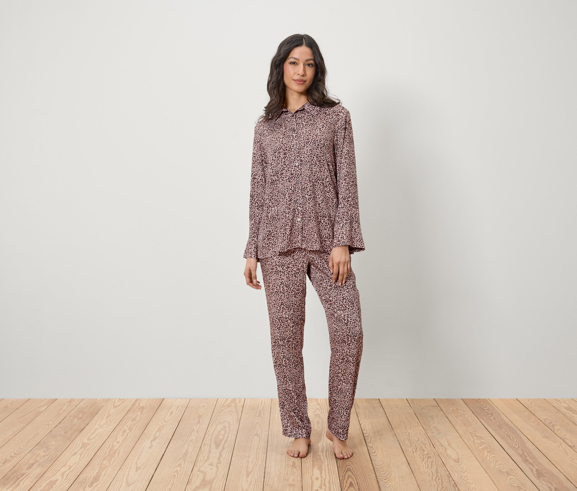 Egy nő áll egy fapadlón és rózsaszín, mintás pizsamát visel.