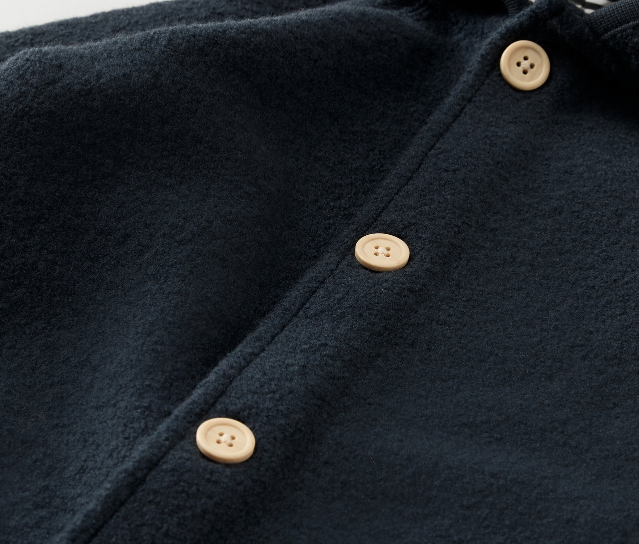 A sötétkék, merinó gyapjú babaruha részlete világos gombokkal.