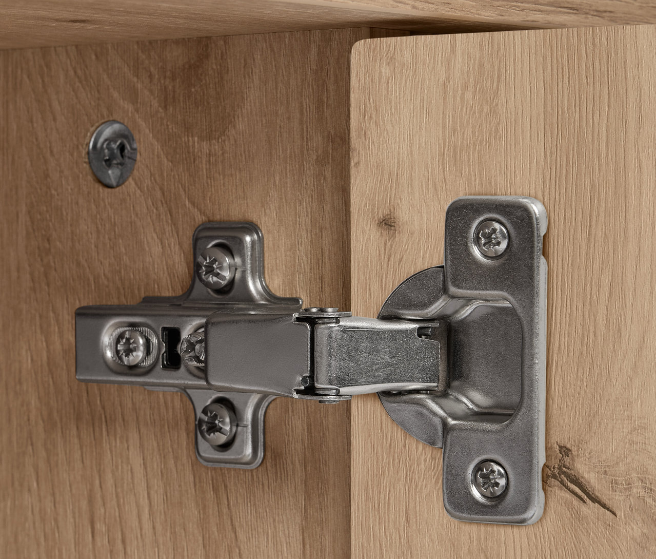 Egy ezüst színű zsanér részlete egy fa REET tálalószekrényen.