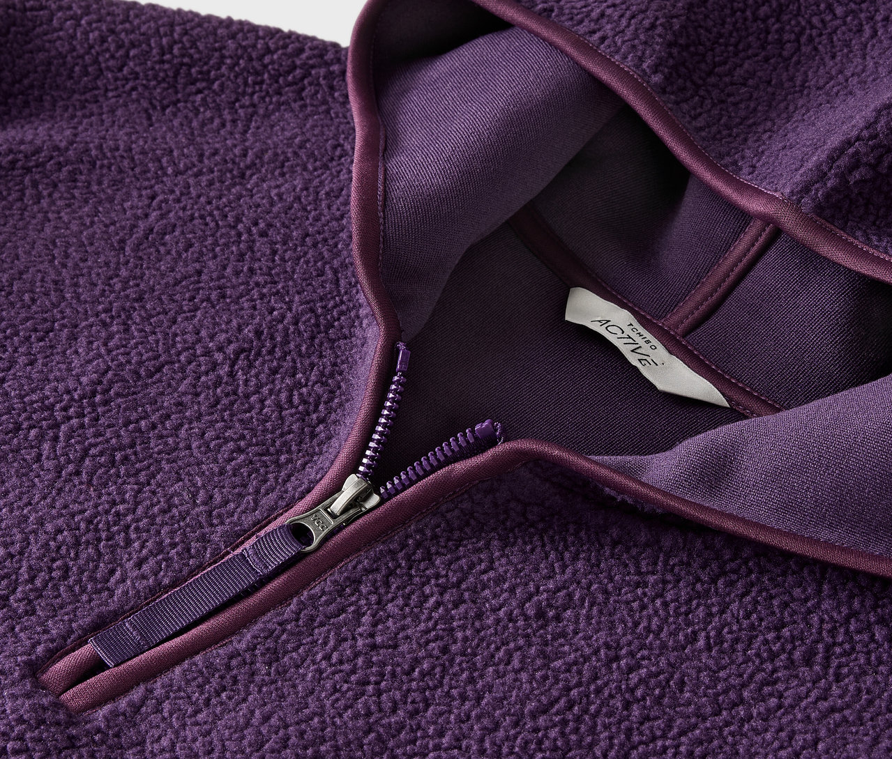 Lila színű, cipzáros, fleece pulóver részlete, címkével.