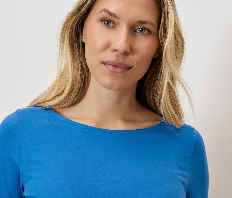 Portré egy szőke nőről kék, hosszú ujjú felsőben.