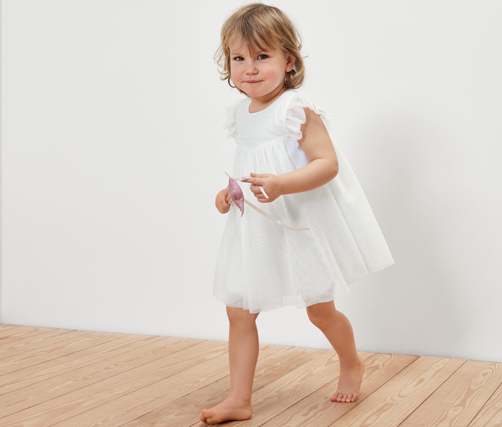 Kisgyerek tüllruhában sétál a fapadlón.