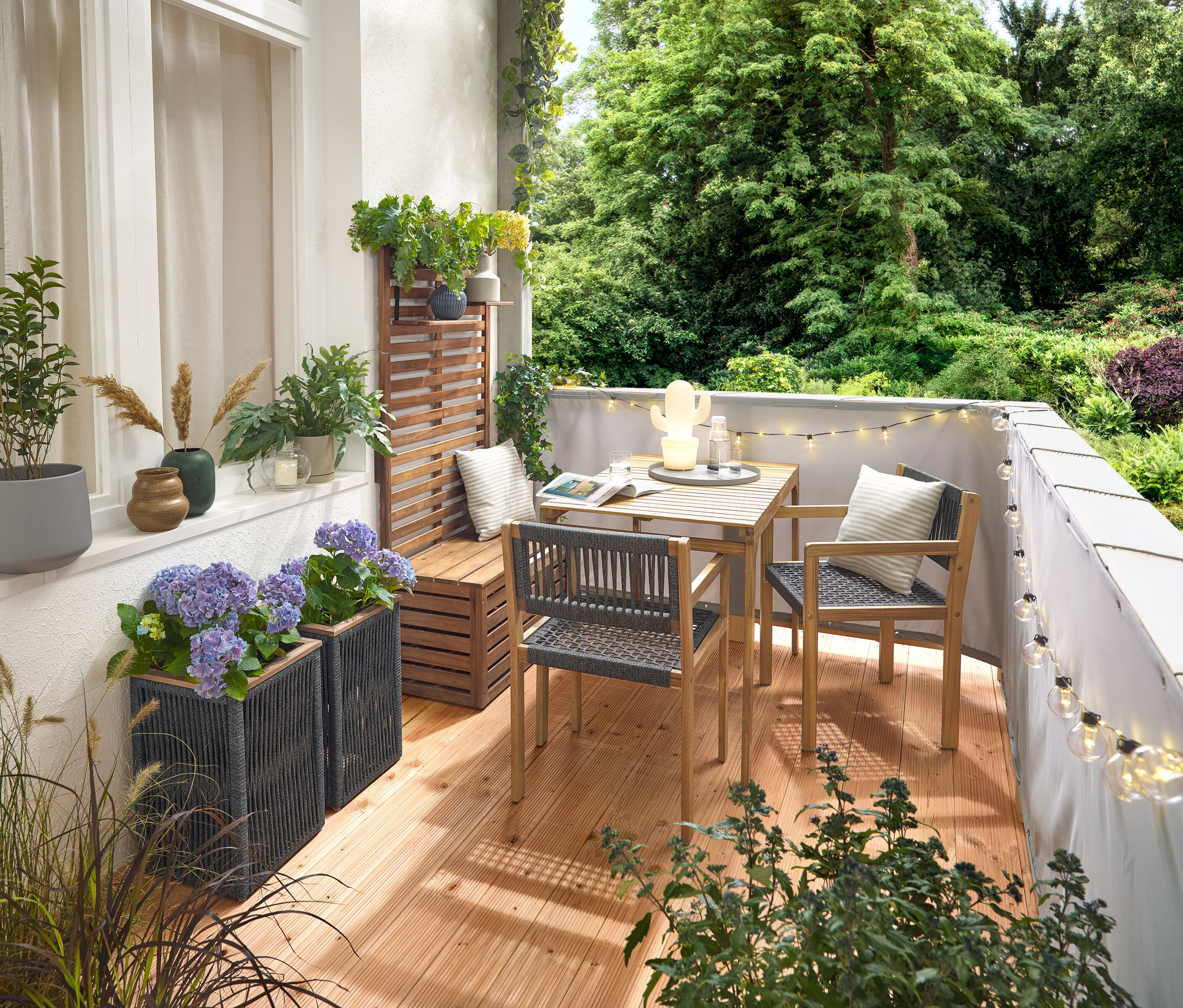 Erkély berendezése textilfonatos erkélygarnitúrával, szürke erkély belátásgátlóval és szélvédővel, LED-es kültéri fényfüzérrel hálózati adapterrel, textilfonatos virágcseréppel, LED-es kültéri akkumulátoros asztali lámpával, kaktusszal és 2 vászonhatású kültéri párnával.