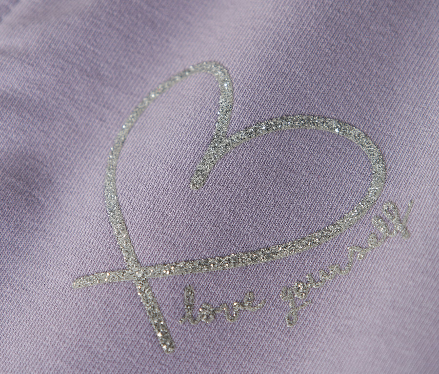 Lila ruhadarab közelképe csillogó szívmintával és a "love yourself" szöveggel.