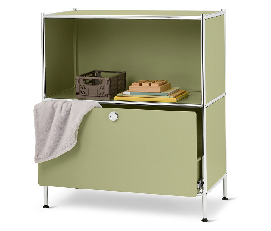 Egy zöld szekrény nyitott felső résszel, amelyben egy barna doboz, könyvek és fa építőkockák találhatók. A fiókon egy szürke kendő lóg.