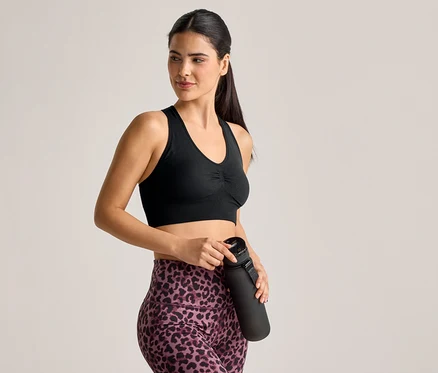 Sportmelltartót és leopárdmintás leggingset viselő nő fekete kulacsot tart.