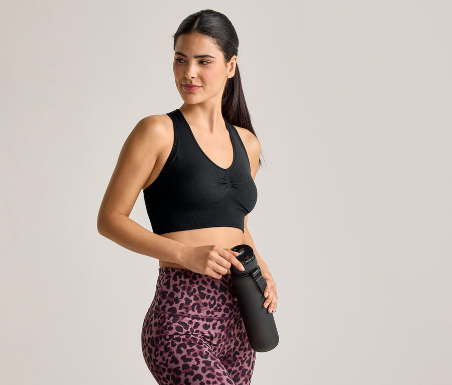 Sportmelltartót és leopárdmintás leggingset viselő nő fekete kulacsot tart.