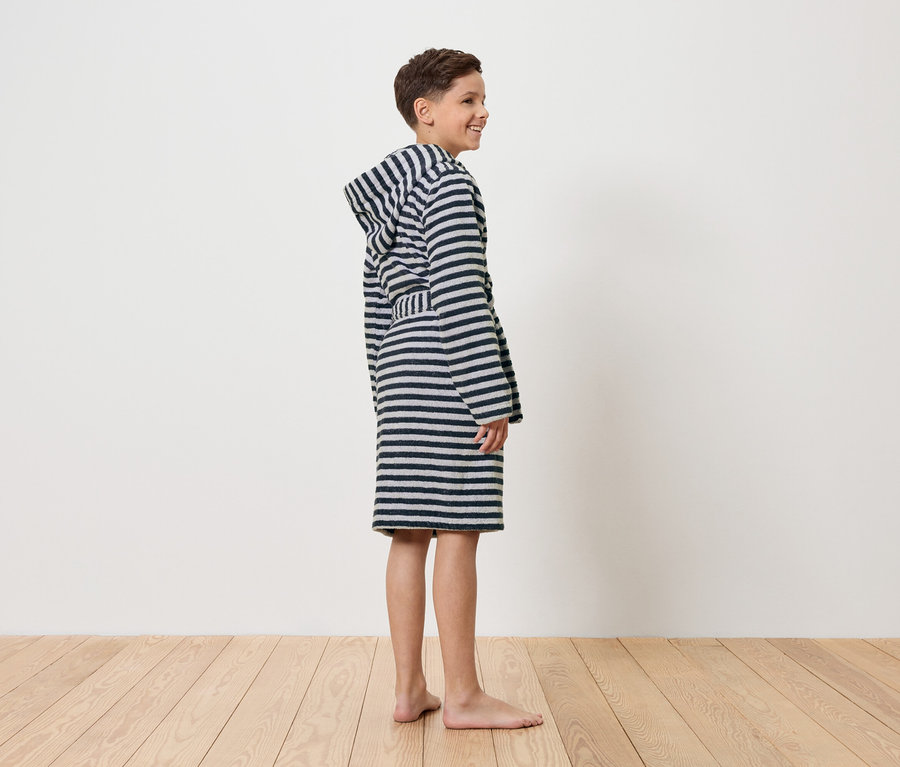 Egy fiú mezítláb áll egy csíkos fürdőköpenyben.