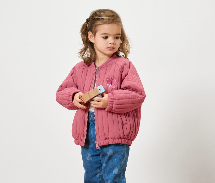 Rózsaszín kabátos lány fából készült játékot tart a kezében.